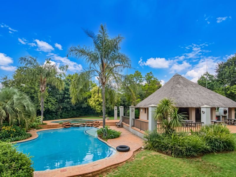 Outdoor entertainment area featuring a swimming pool with a rock water feature and a spacious thatched lapa for social gatherings.