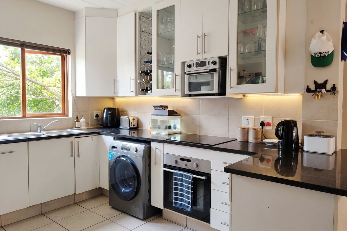 A well-maintained kitchen featuring white cabinetry, granite countertops, integrated oven and microwave, and under-cabinet lighting with a view of the outdoors.
