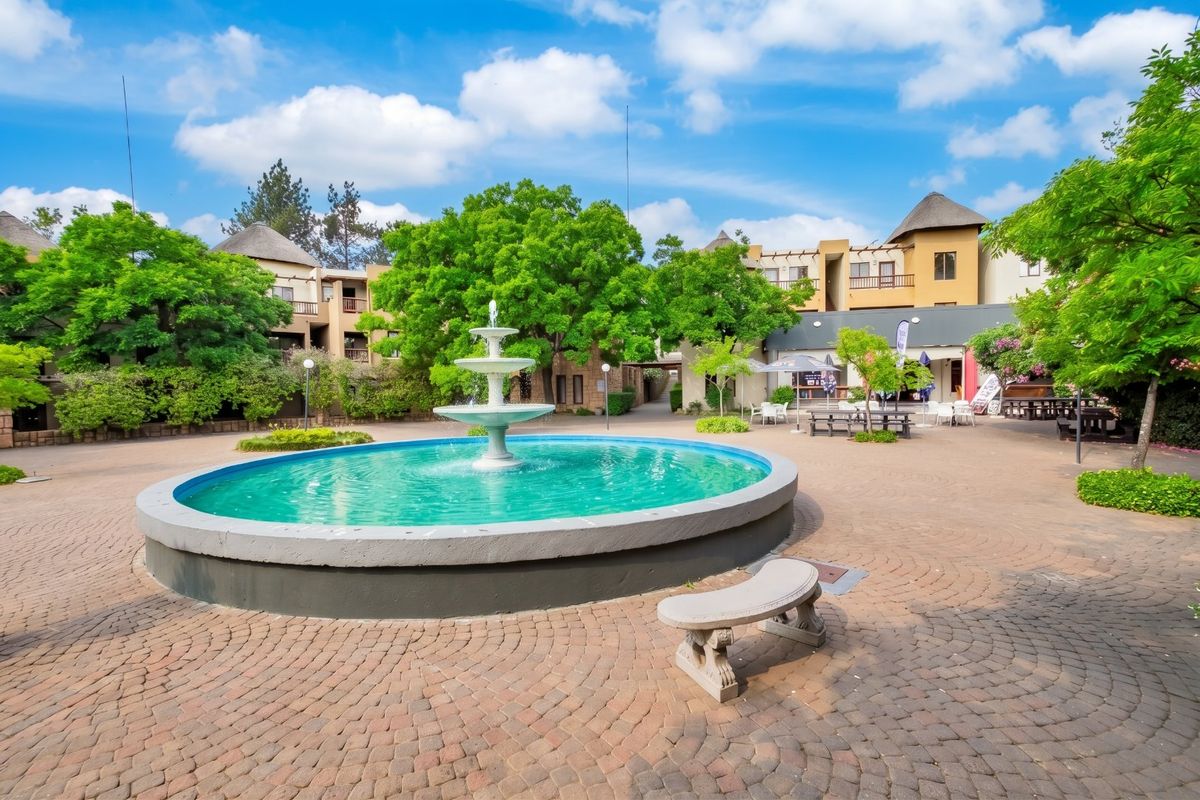 A well-maintained communal courtyard featuring a central water fountain, paved walkways, and mature trees within an apartment complex setting.