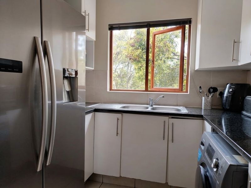A functional kitchen featuring white cabinetry, granite countertops, a double bowl stainless steel sink, and a window overlooking greenery.