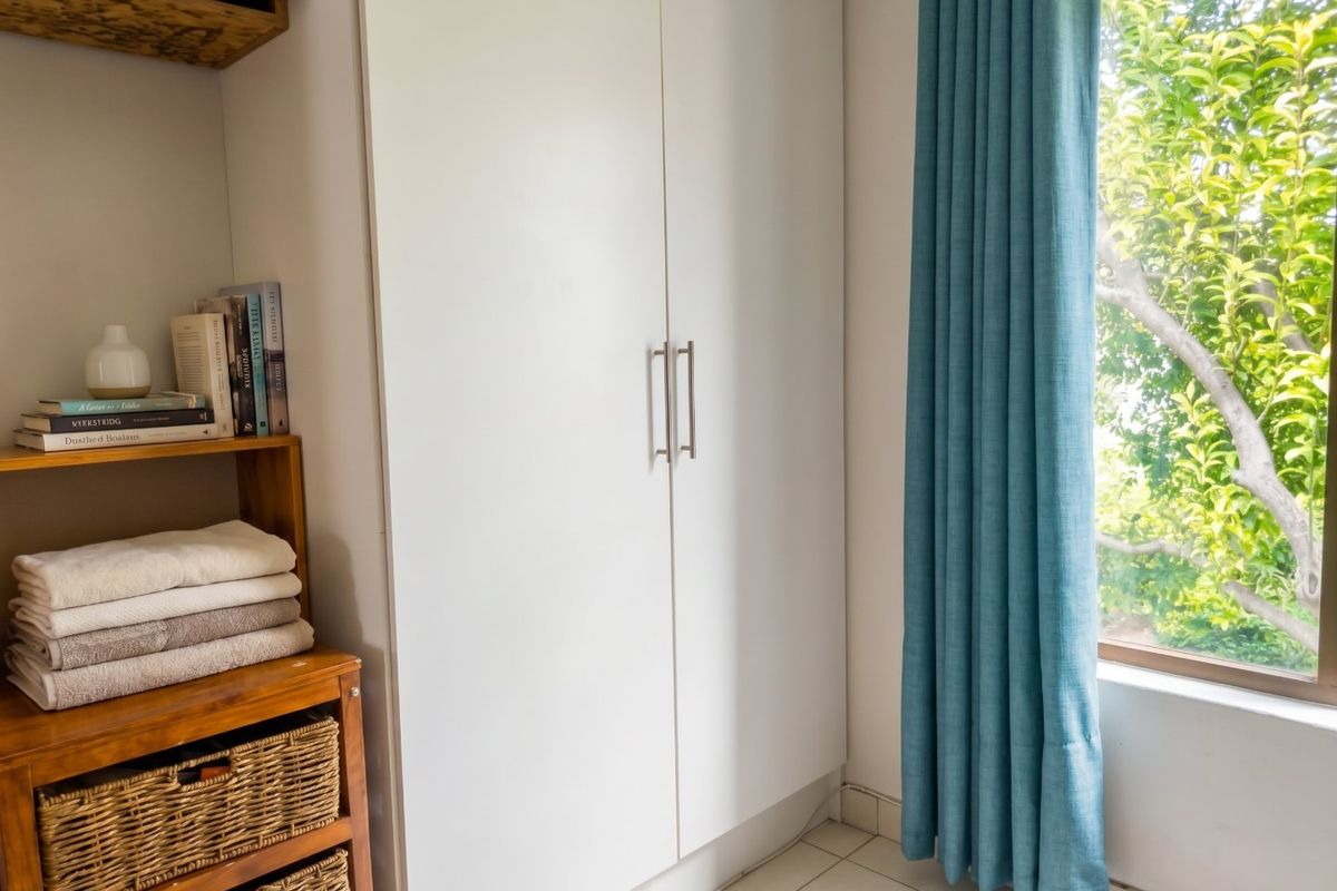 A bedroom featuring a built-in wardrobe with modern handles, tiled flooring, and a window with natural light.