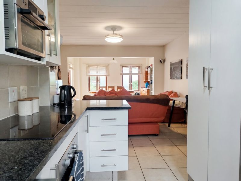 Open-plan kitchen and living area featuring modern white cabinetry, granite countertops, built-in oven, hob, and tiled flooring throughout the space.