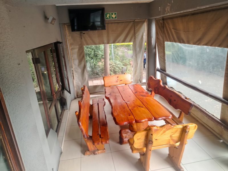 A covered patio area featuring tiled flooring, sliding glass doors, and roll-up canvas blinds, providing a functional outdoor entertainment space.