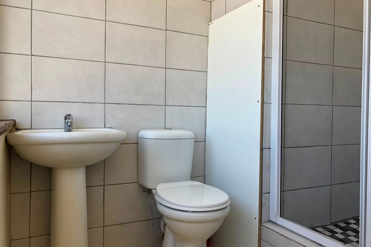 A functional bathroom featuring a pedestal basin, toilet, and shower enclosure with neutral wall tiling. The space requires cosmetic updates to improve finish quality.