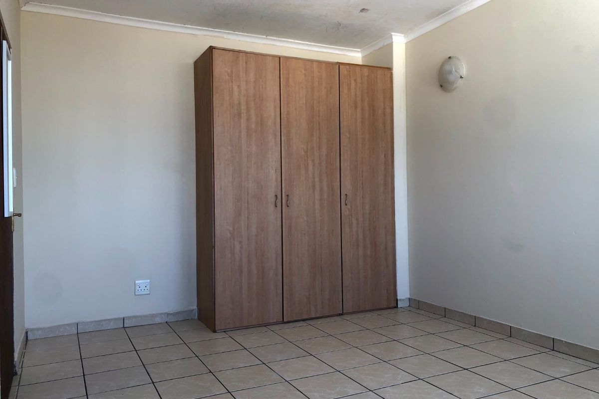 An empty bedroom featuring tiled flooring and a built-in wooden wardrobe, requiring minor cosmetic updates to the walls and ceiling.