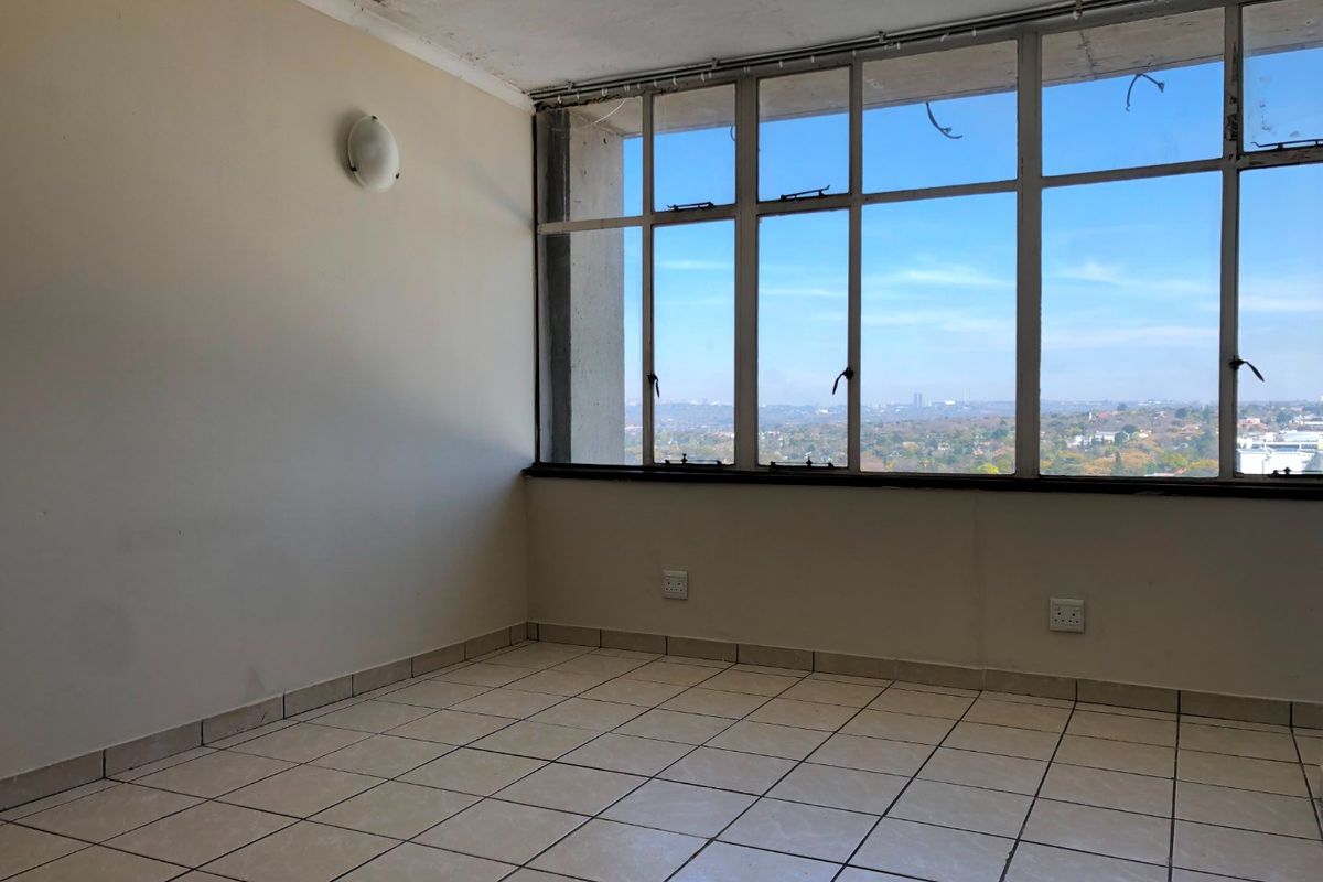 An empty living area featuring tiled flooring, large windows with expansive views, and wall-mounted lighting, requiring some cosmetic attention to the ceiling and window frames.