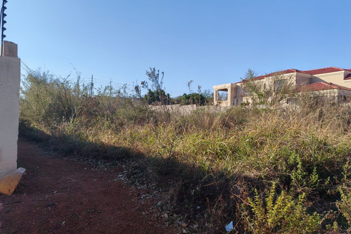 A vacant residential plot featuring overgrown vegetation, perimeter walling, and existing electric fencing, situated in a developed neighborhood.
