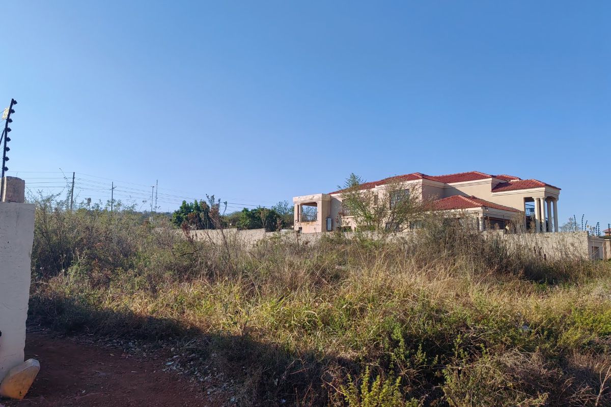 Vacant residential land plot featuring perimeter walling and electric fencing, with surrounding natural vegetation and nearby established residential property.