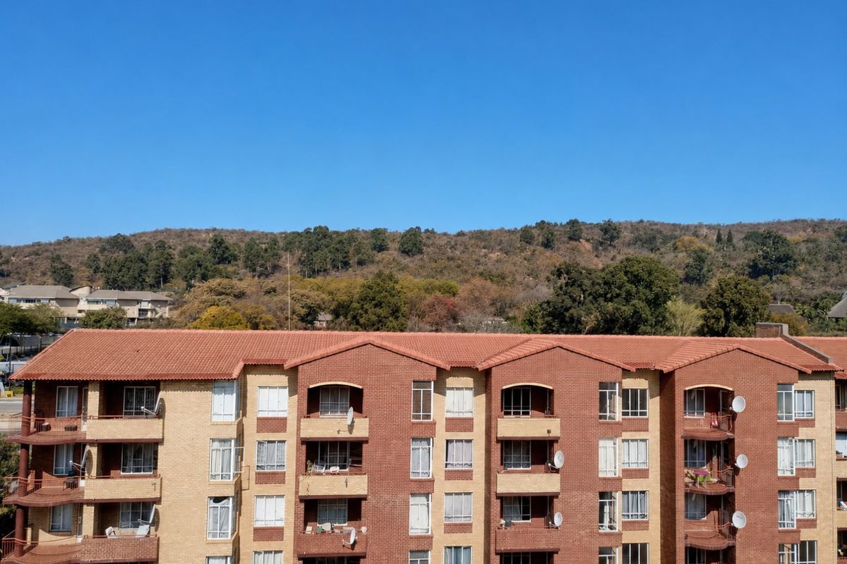 Exterior view of a multi-story apartment building featuring a brick facade, tiled roof, and private balconies with scenic hillside views.