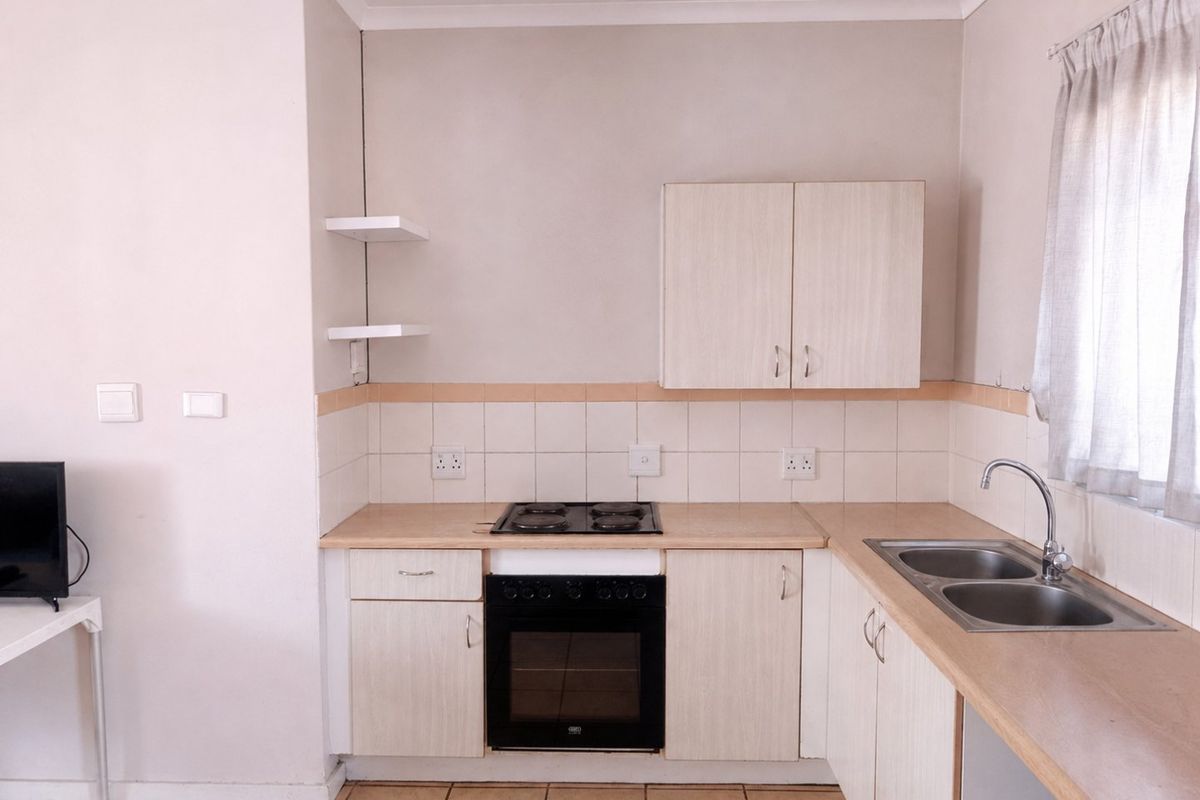 A functional kitchen featuring built-in cabinetry, laminate countertops, an electric hob, an oven, and a double bowl stainless steel sink with tiled backsplash.