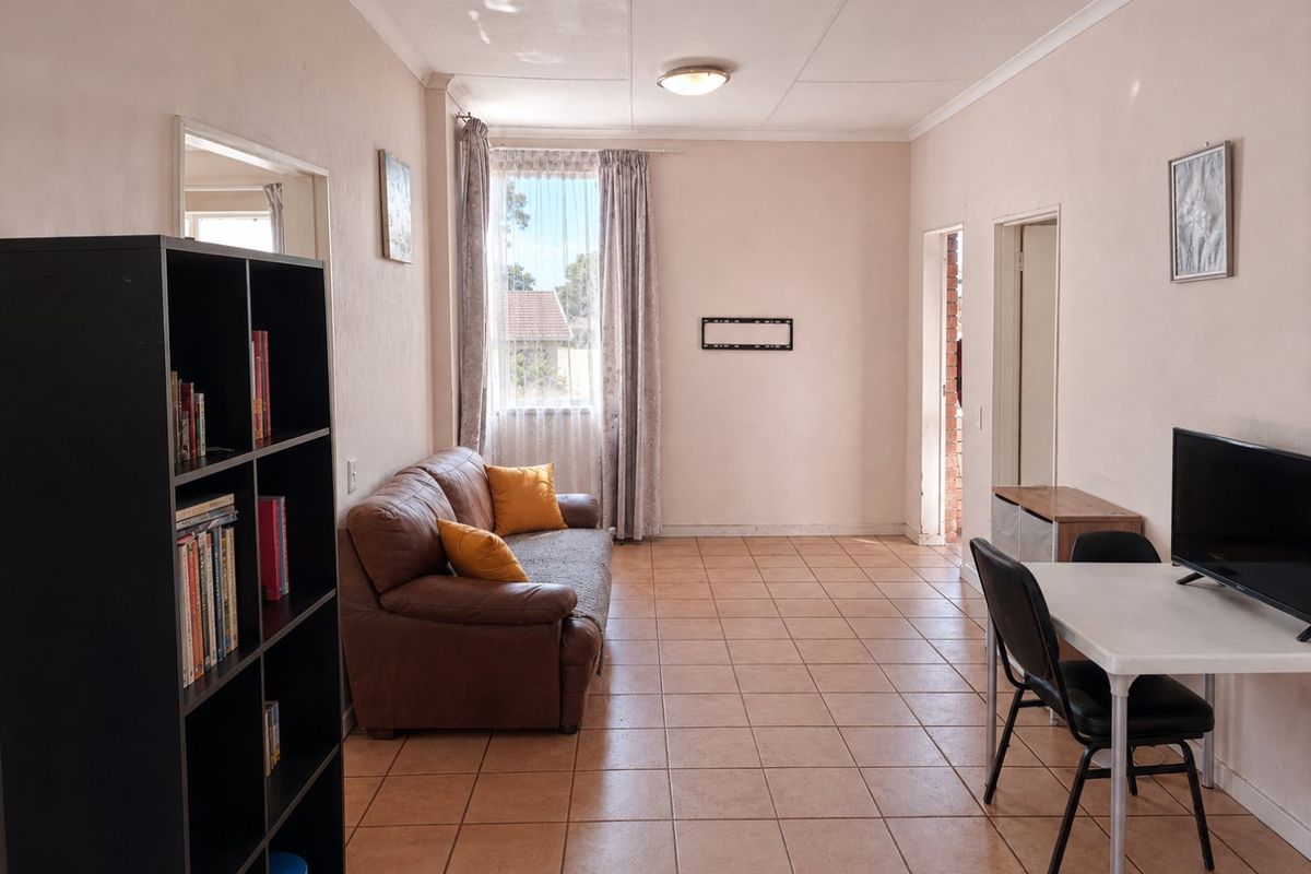 A living area featuring tiled flooring and neutral wall finishes, offering a functional space with direct access to adjacent rooms.