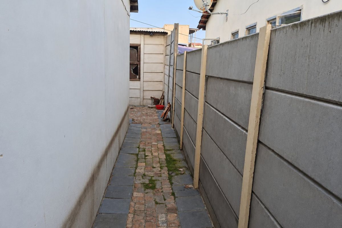 A narrow side passage featuring a precast concrete boundary wall and a combination of brick and stone paving leading to the rear area.