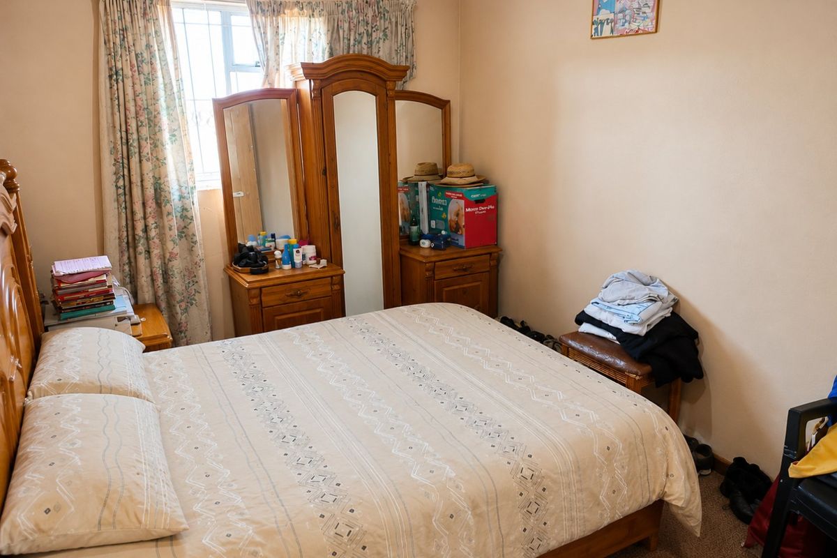 A standard bedroom featuring carpeted flooring, coving, and a window fitted with security bars.