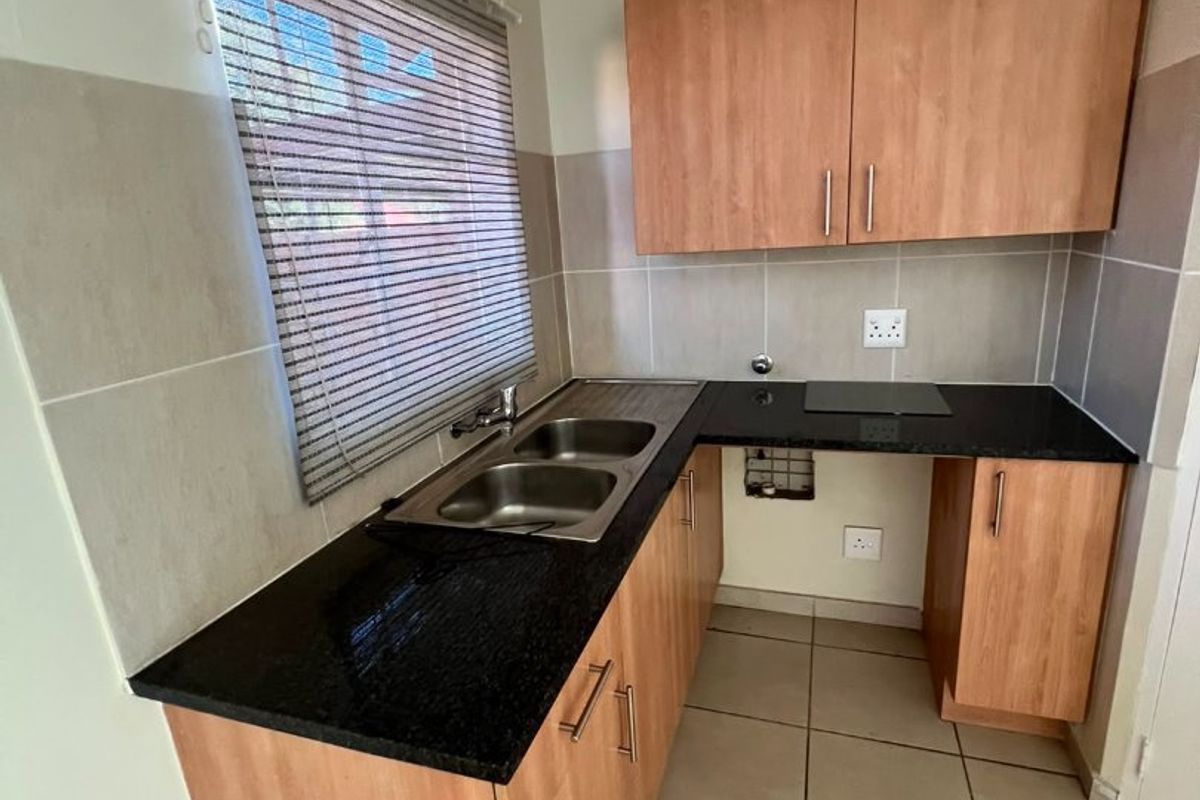 A compact kitchen featuring laminate cabinetry, granite countertops, a stainless steel double sink, and neutral tiled splashbacks with ceramic floor tiles.
