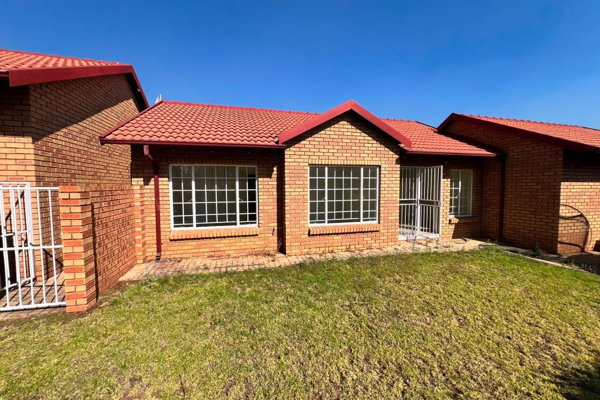 Rear view of a face brick apartment featuring a tiled roof, security gates, and grid windows overlooking a private lawn area.