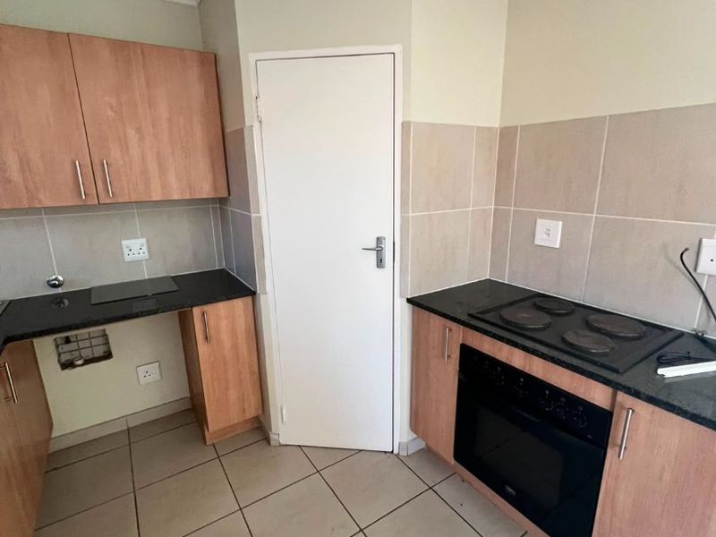 A functional kitchen featuring built-in cabinetry, laminate countertops, an integrated electric hob and oven, and tiled flooring. The space is currently vacant.