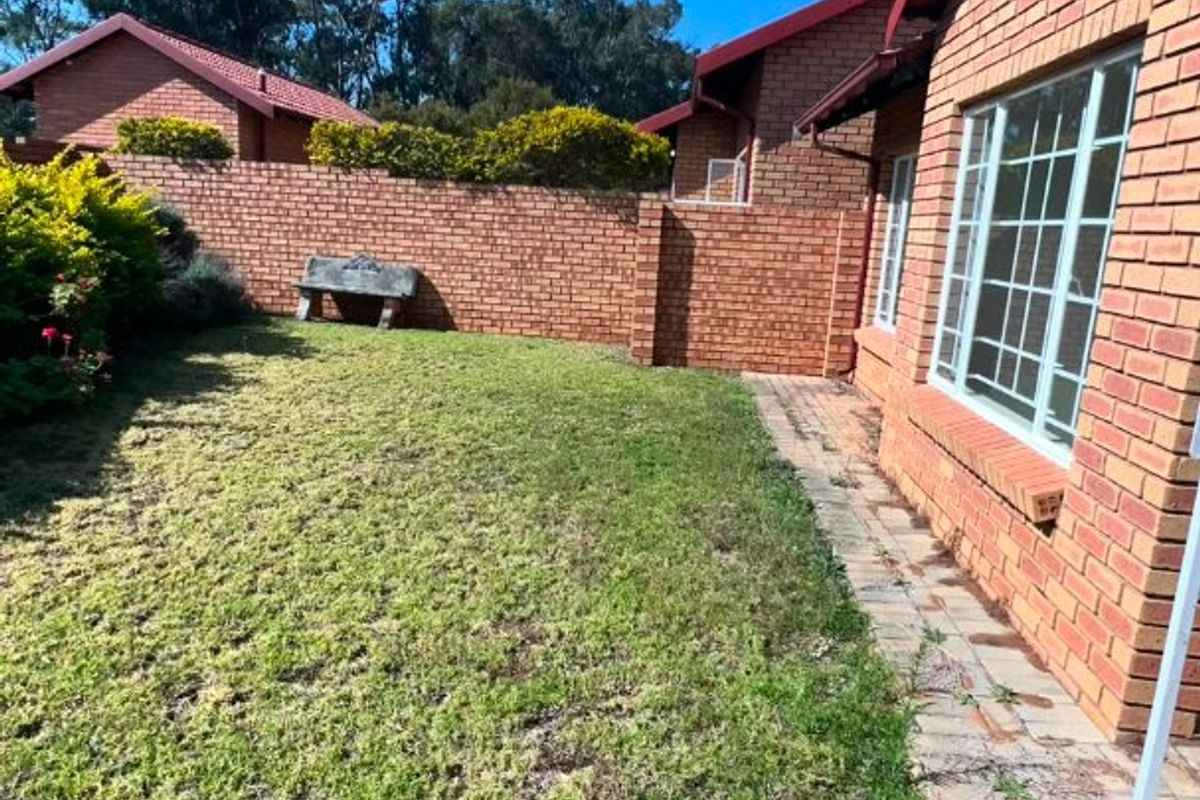 A private rear garden featuring a well-maintained lawn, paved walkway, and secure perimeter brick walling adjacent to the apartment building.