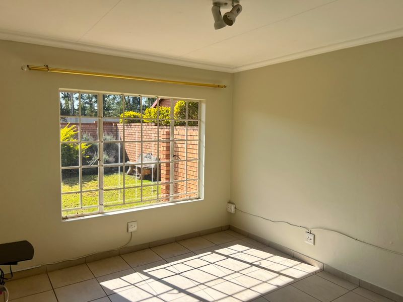 A bright, empty bedroom featuring tiled flooring, security bars on the window, and a ceiling-mounted light fixture.