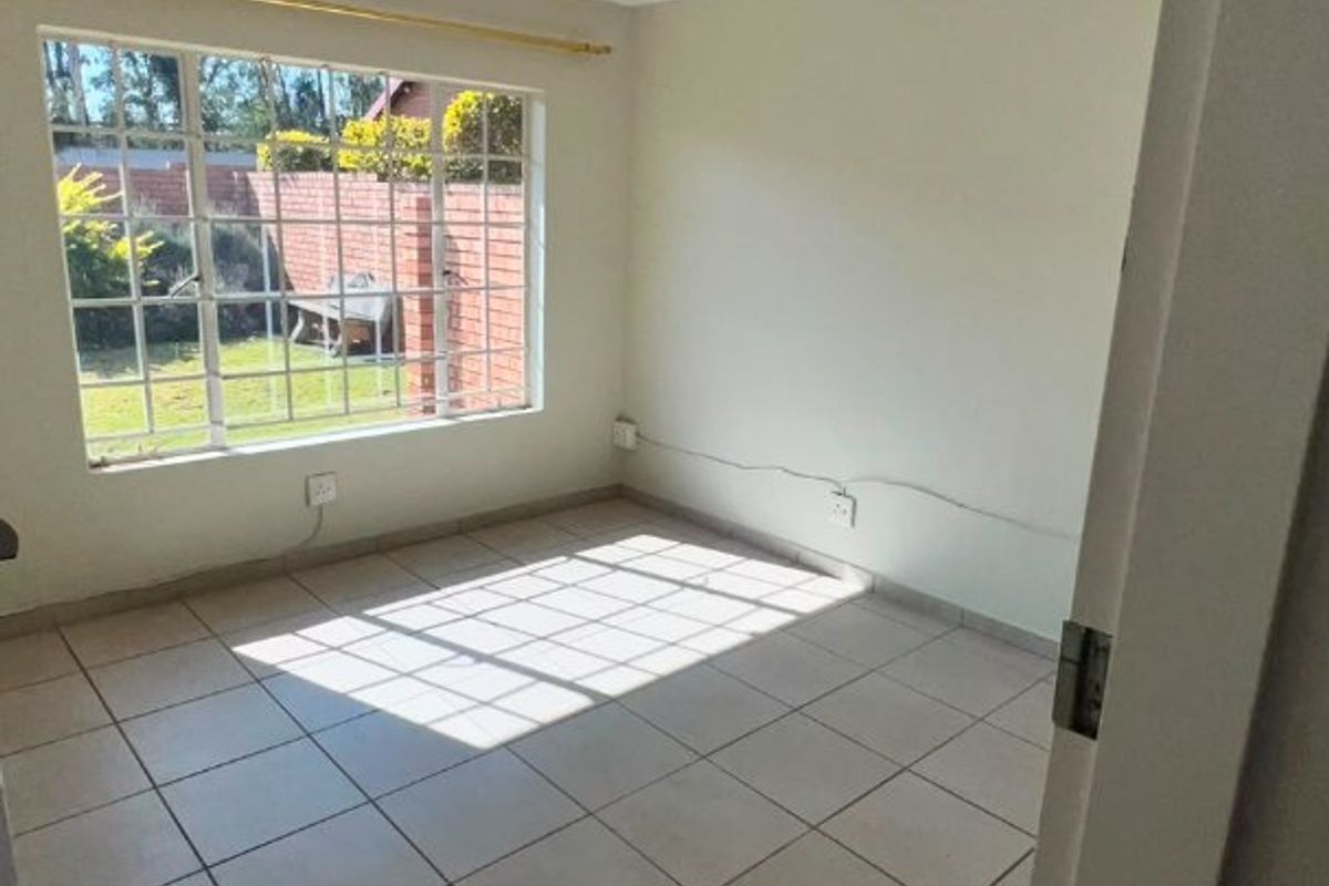 A bright, empty bedroom featuring neutral tiled flooring, a large grid-pattern window, and simple ceiling lighting, offering a clean canvas for personalization.