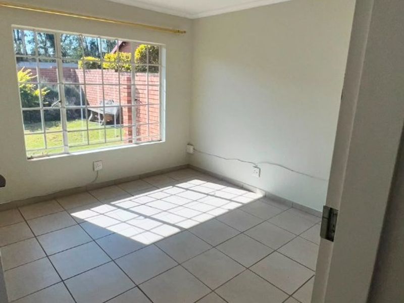 A bright, empty bedroom featuring neutral tiled flooring, a large grid-pattern window, and simple ceiling lighting, offering a clean canvas for personalization.