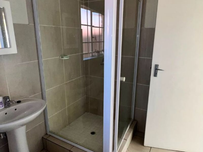 A functional bathroom featuring a pedestal basin and a corner shower enclosure with tiled walls and flooring.