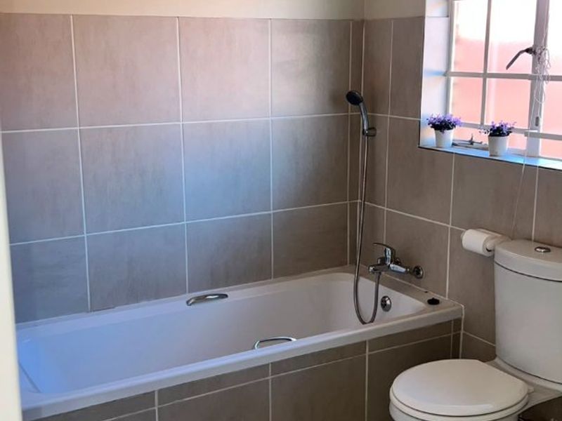 A functional bathroom featuring a bathtub with a shower mixer, a toilet, and neutral wall and floor tiling.