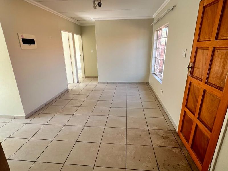 An empty, open-plan living area featuring neutral tiled flooring, a solid wooden door, and a standard electrical distribution board.
