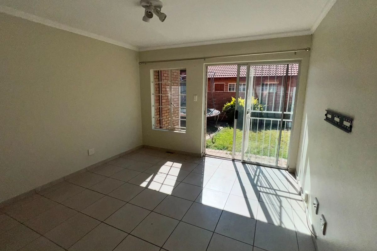 An empty living room featuring tiled flooring, a sliding glass door with security gate, and access to a small rear garden area.