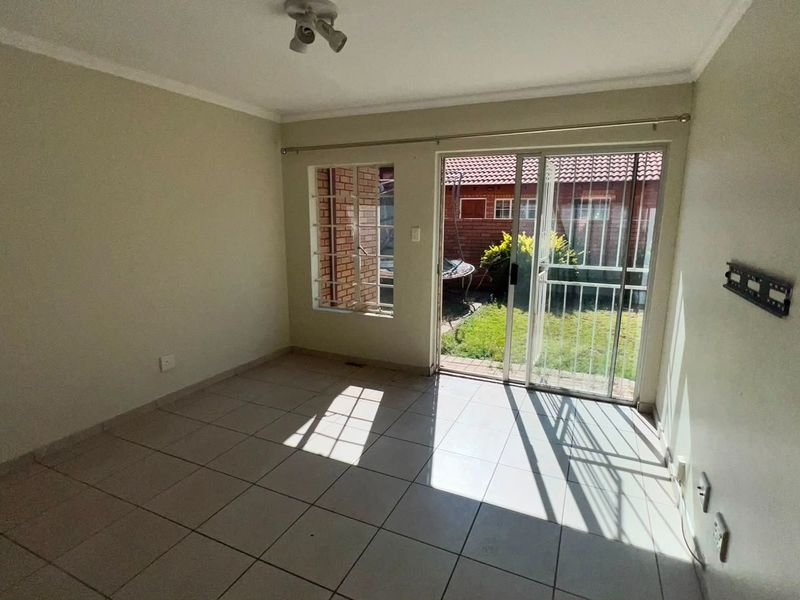 An empty living room featuring tiled flooring, a sliding glass door with security gate, and access to a small rear garden area.