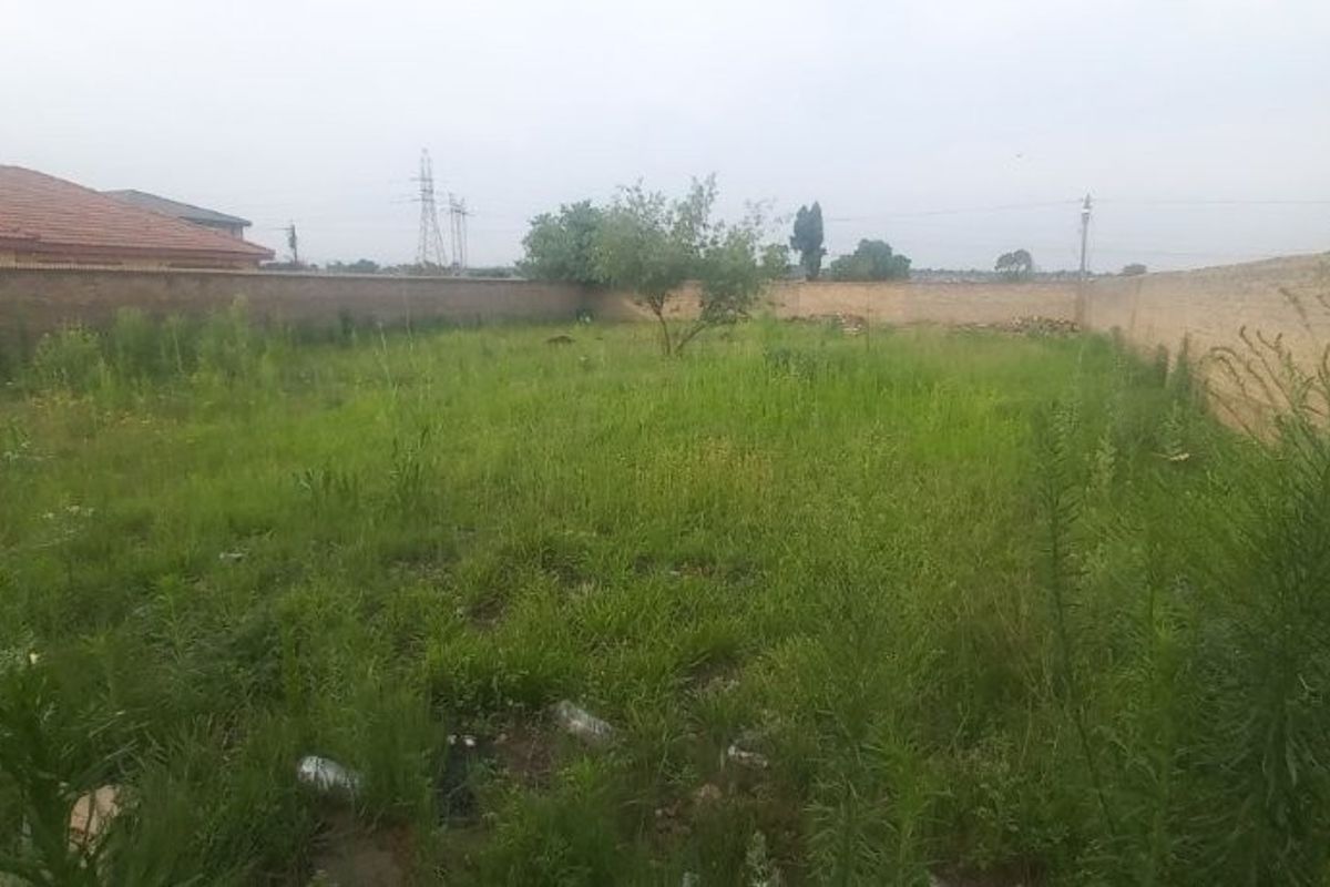 A vacant residential plot featuring a level surface enclosed by perimeter brick walls, currently covered in overgrown grass and vegetation.