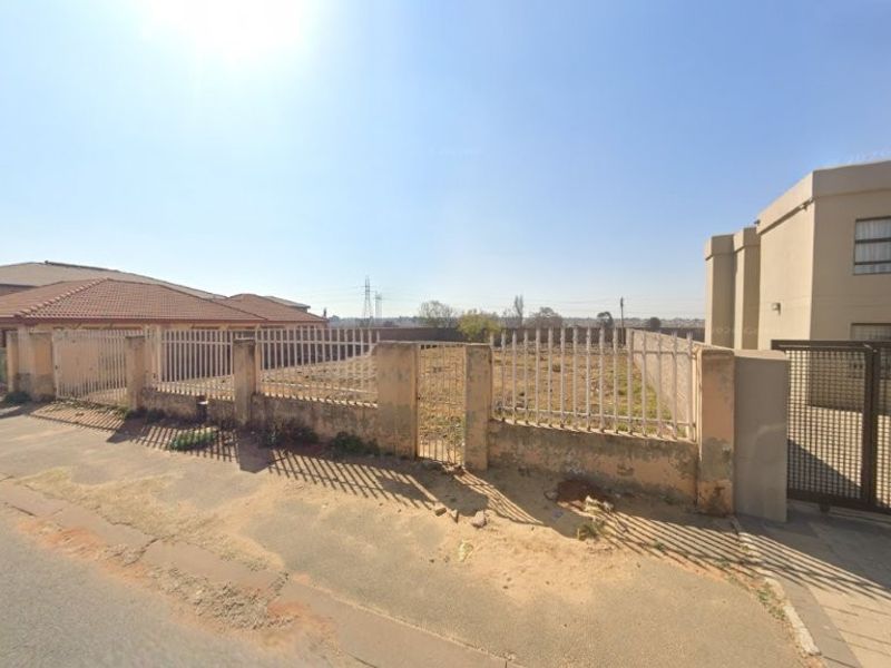 A vacant residential plot enclosed by a perimeter wall and metal fencing, situated between existing residential developments.