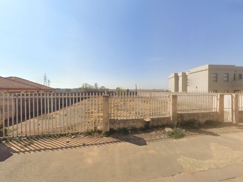 A vacant residential plot enclosed by perimeter fencing and concrete pillars, viewed from the street.