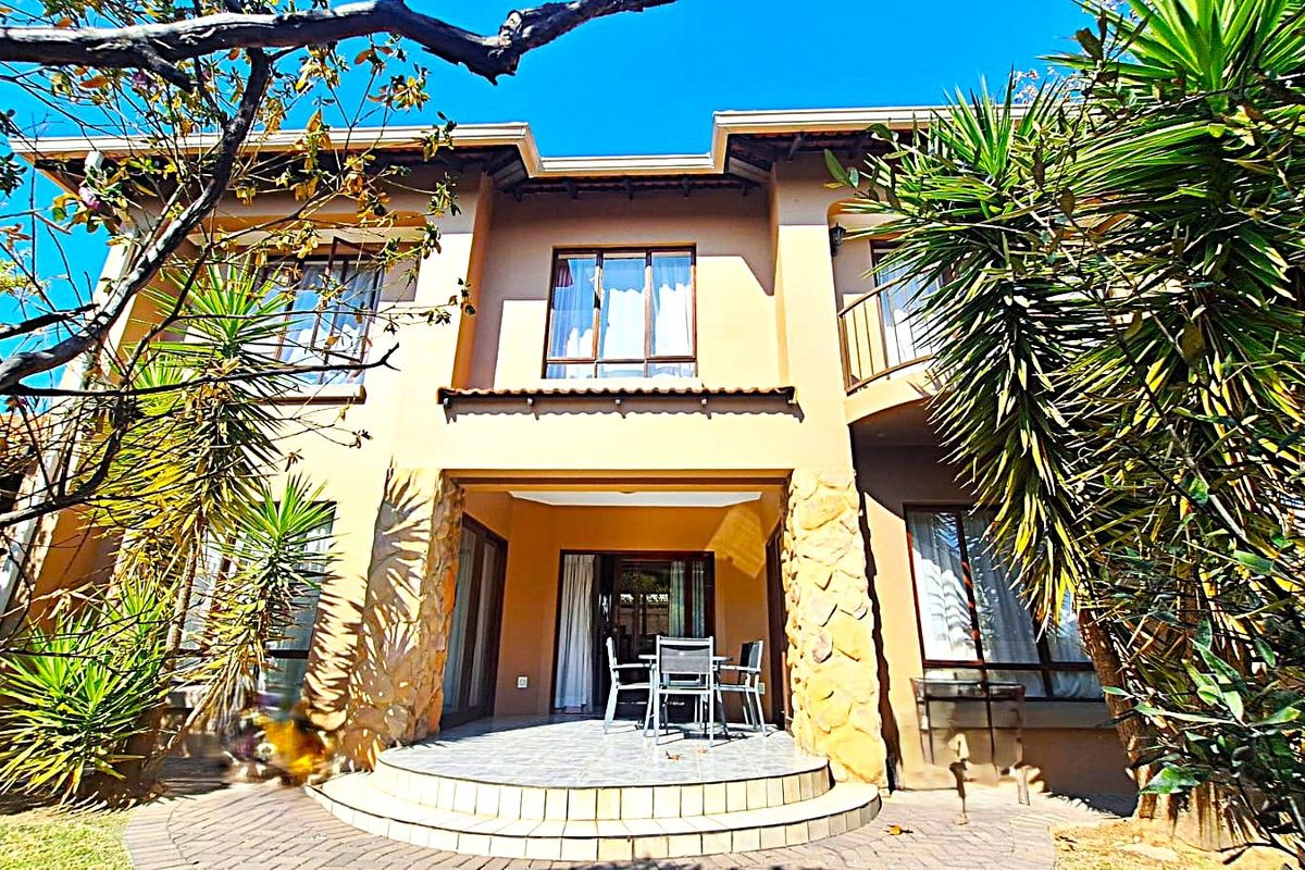 Rear elevation of a two-story house featuring stone cladding accents, a tiled patio area, and a balcony overlooking the garden.