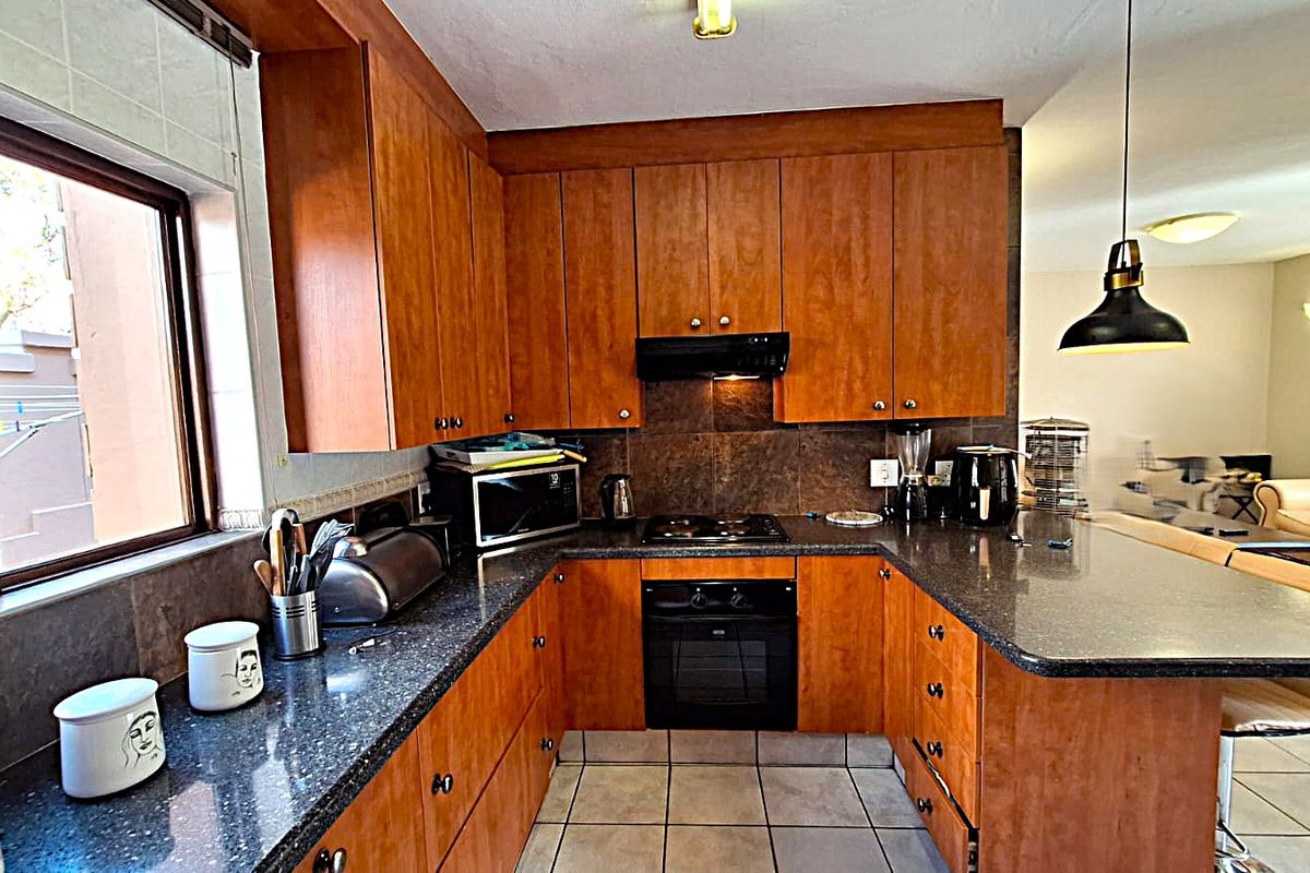 A functional kitchen featuring warm-toned wooden cabinetry, dark granite countertops, a built-in oven, and a breakfast bar overlooking the adjacent living area.