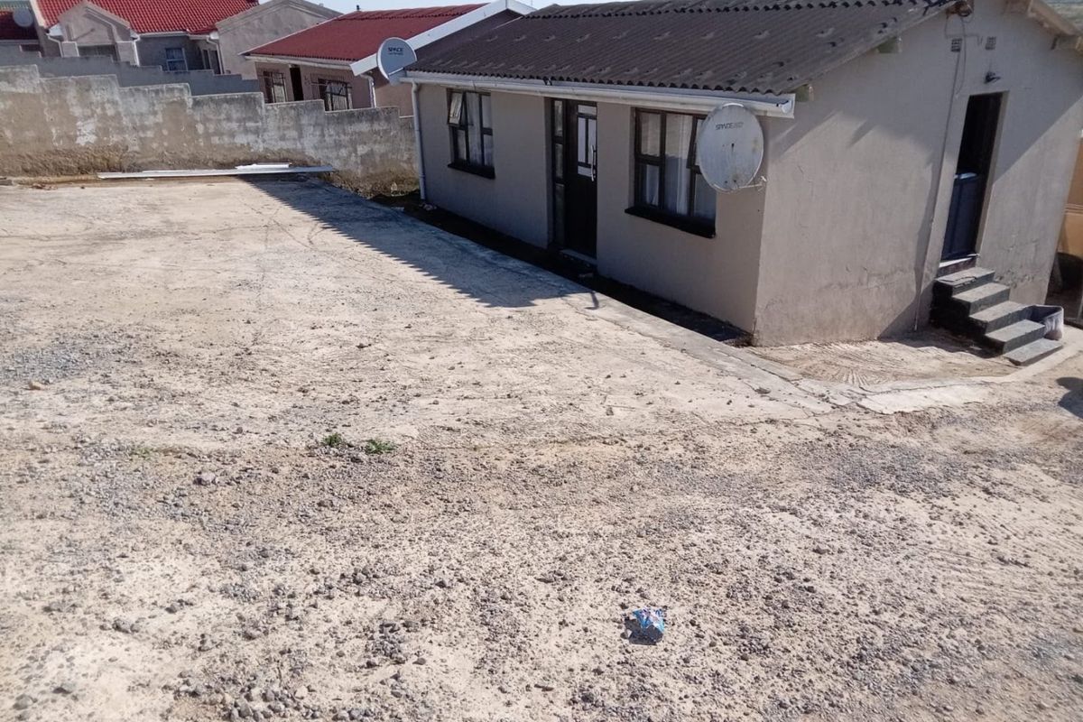 Rear view of the property featuring a large concrete yard area, boundary wall, and exterior access steps to the dwelling.