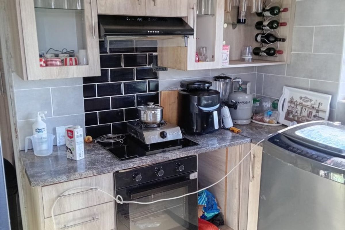 Compact kitchen featuring light wood-look cabinetry, a built-in oven, extractor fan, and a contrasting black tiled backsplash.
