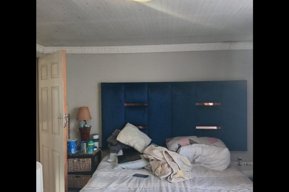 A bedroom featuring a blue upholstered headboard, ceiling cornice detailing, and a flush mount light fixture. The ceiling shows signs of wear and staining.