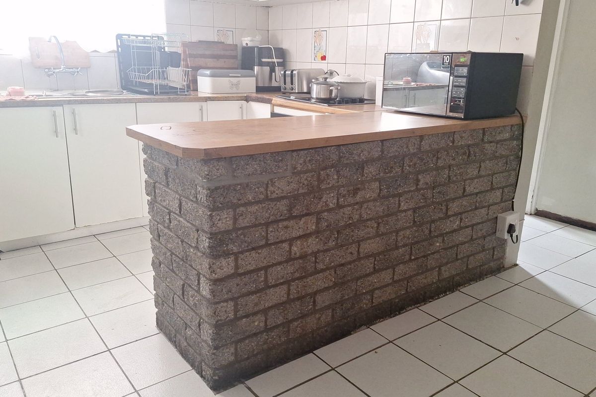 A functional kitchen featuring a distinctive brick breakfast bar, laminate countertops, tiled backsplash, and ceramic floor tiles with ample built-in cabinetry.