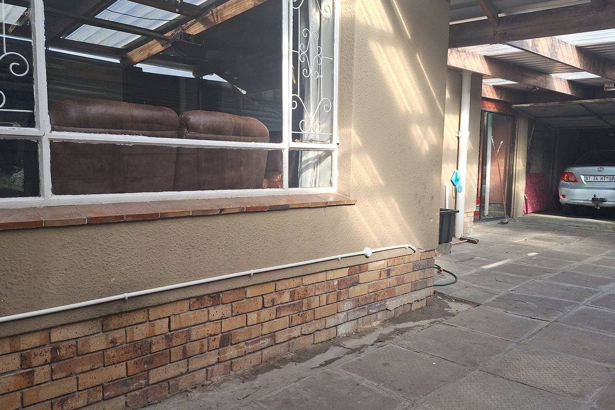 Rear exterior view showing a covered patio area with brick plinth, paved flooring, and security bars on the windows.