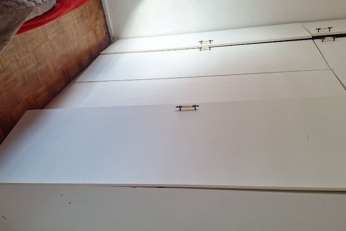 A bedroom featuring built-in white cupboards and traditional parquet flooring, showing signs of wear and tear.