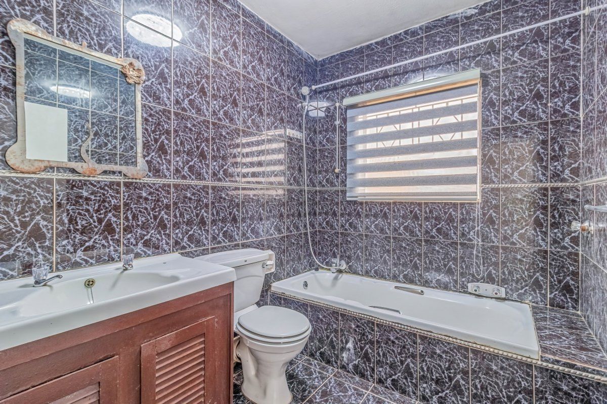 A functional bathroom featuring dark marble-effect wall and floor tiles, a built-in bathtub, a vanity cabinet with basin, and a toilet.