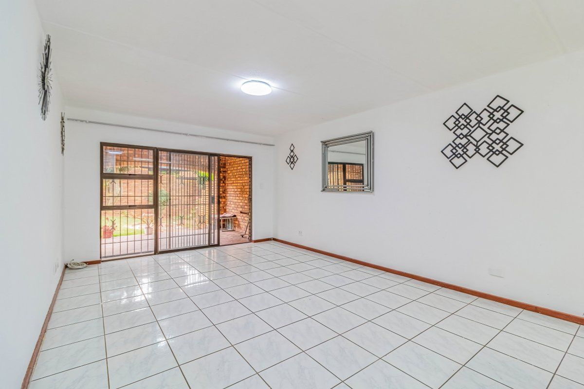 A bright, empty living room featuring white tiled flooring and a sliding glass door with a security gate leading to an outdoor area.