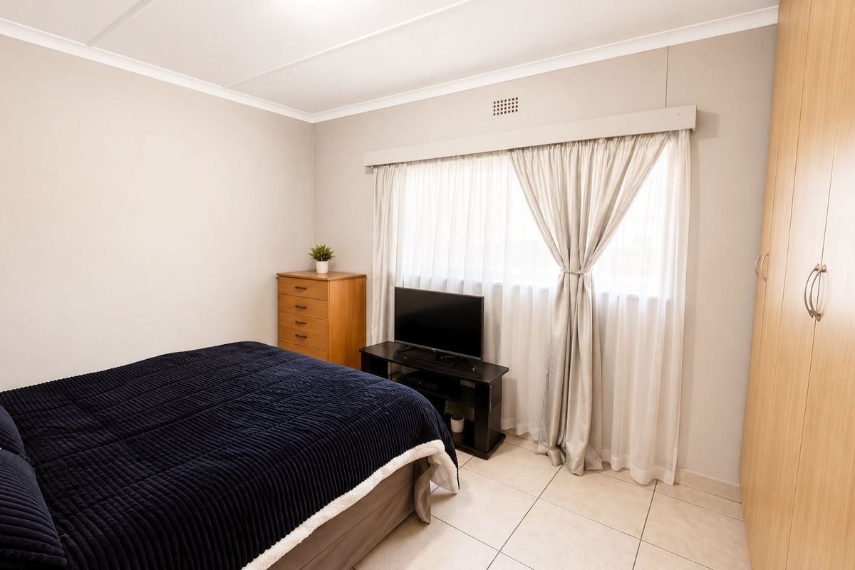 A well-maintained bedroom featuring neutral wall tones, tiled flooring, and a large built-in wardrobe providing ample storage space.