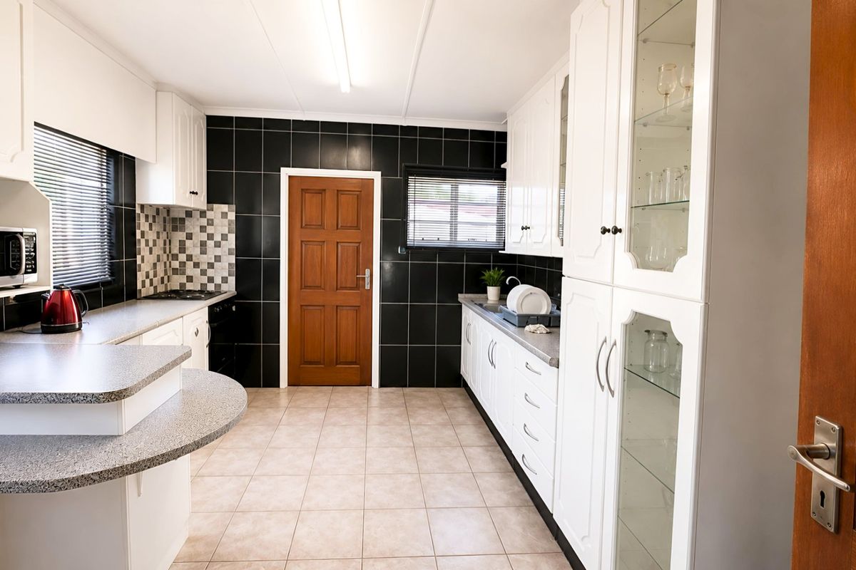 A functional kitchen featuring white cabinetry, contrasting black tiled splashbacks, laminate countertops, and tiled flooring with ample storage space.