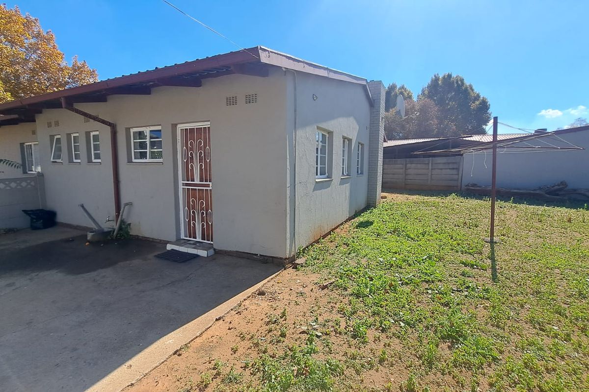 Rear view of the property featuring a concrete driveway, security gate, and a spacious backyard with a rotary clothesline and perimeter walling.