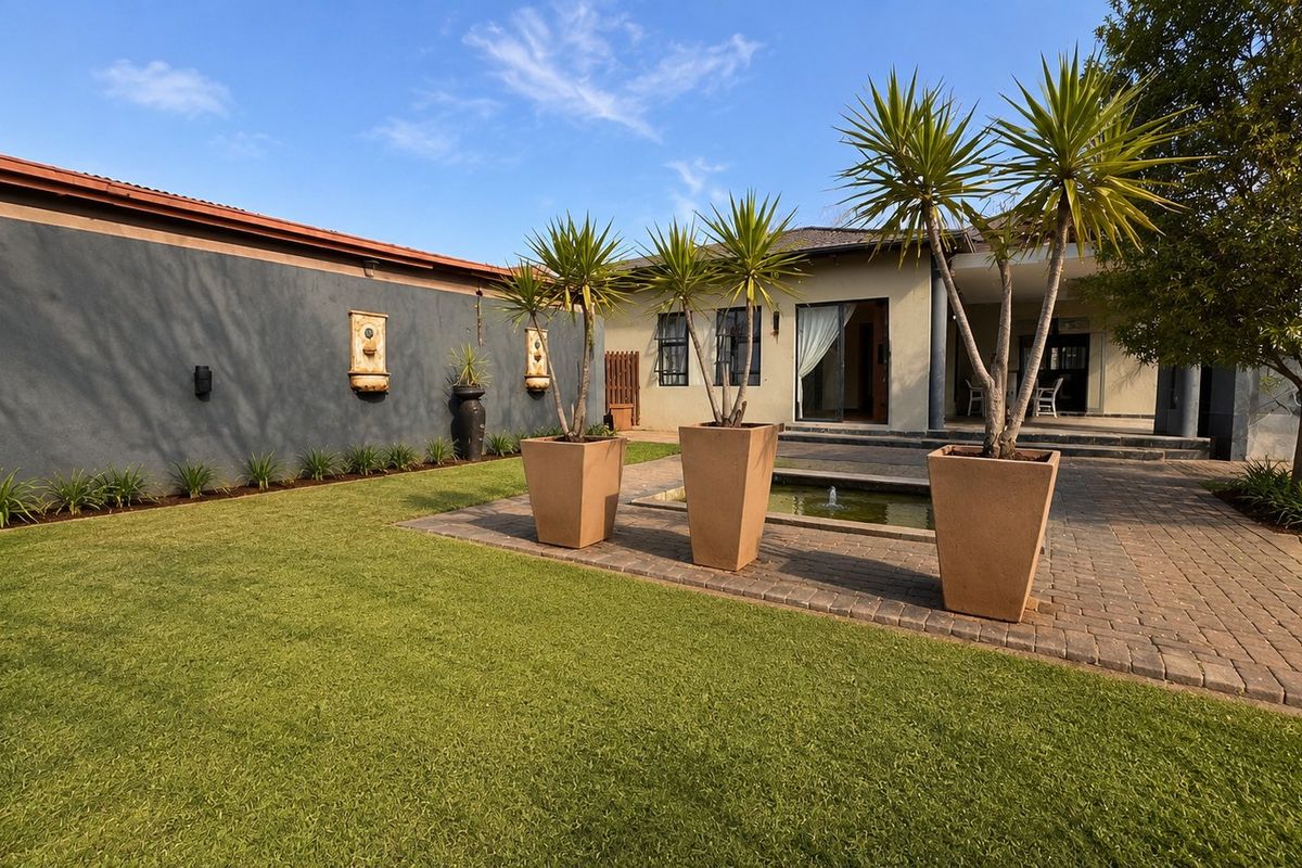 A well-maintained rear garden featuring a paved patio area, a small water feature, and wall-mounted fountains, providing a pleasant outdoor entertainment space.