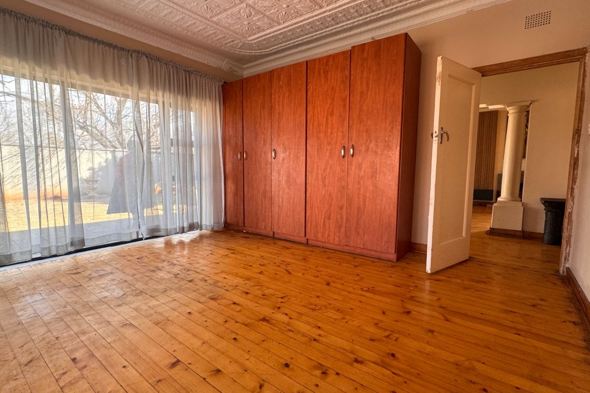 Spacious bedroom featuring original timber flooring, classic pressed metal ceiling, and built-in wooden cupboards with direct access to the garden.