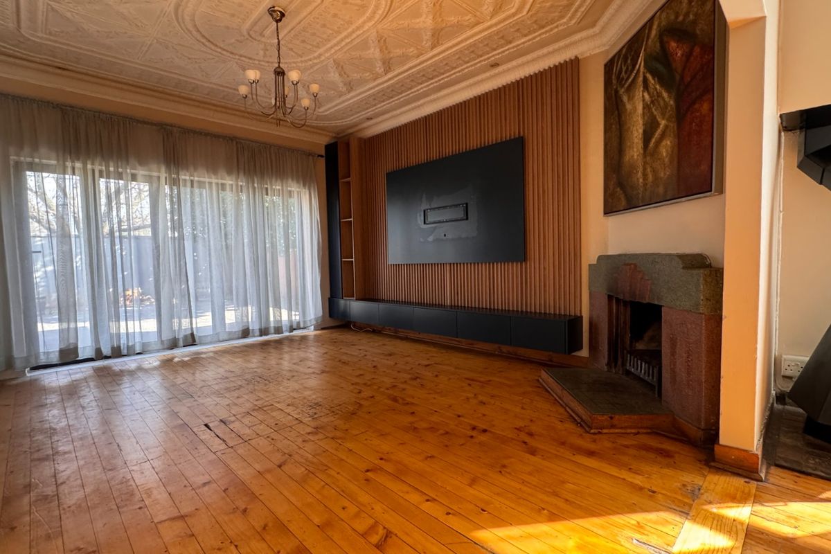 Spacious living room featuring original timber flooring, an ornate pressed metal ceiling, a stone fireplace, and a modern timber slat media wall.