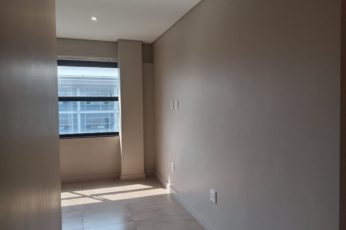 A bright, empty bedroom featuring neutral wall tones, tiled flooring, and a large window providing natural light.