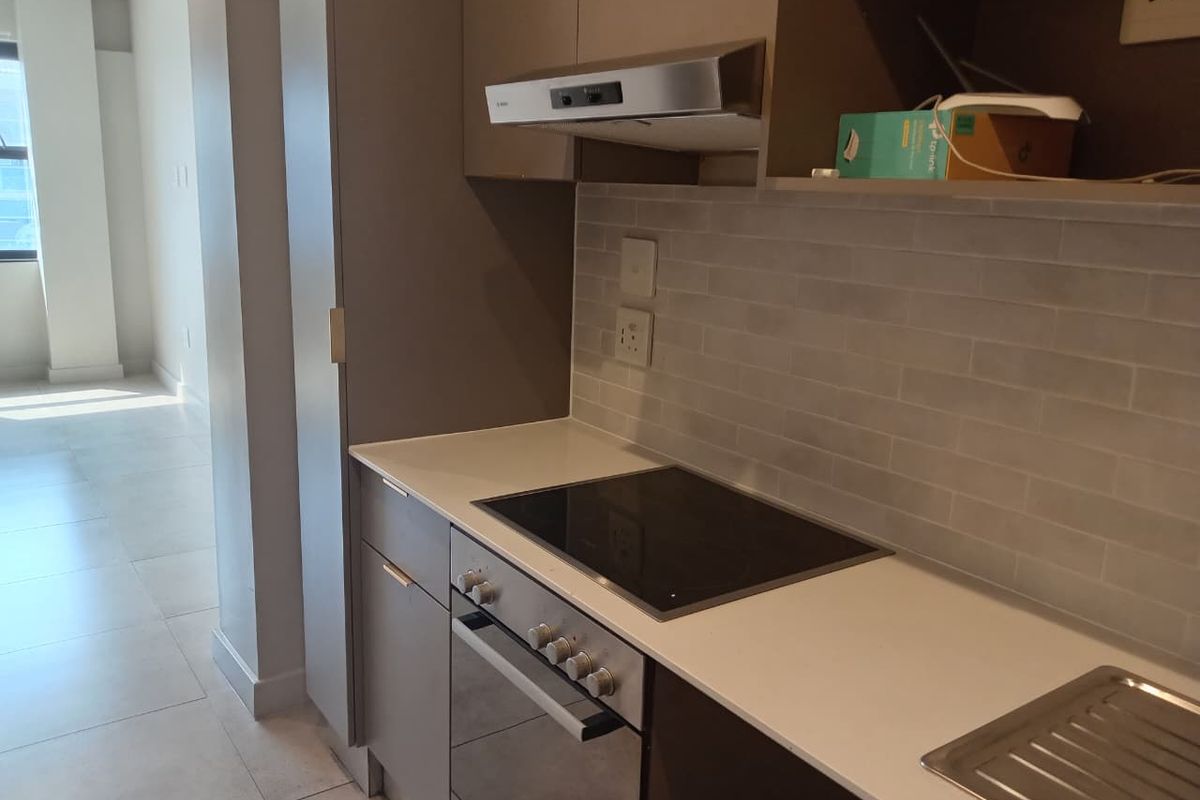 Modern kitchen featuring sleek grey cabinetry, stone countertops, a built-in oven, electric hob, and a stylish subway tile backsplash.